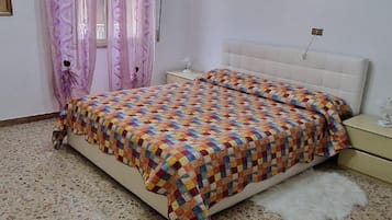 Una camera da letto con un letto, un comodino, un tappeto bianco e soffice e una finestra con tende.