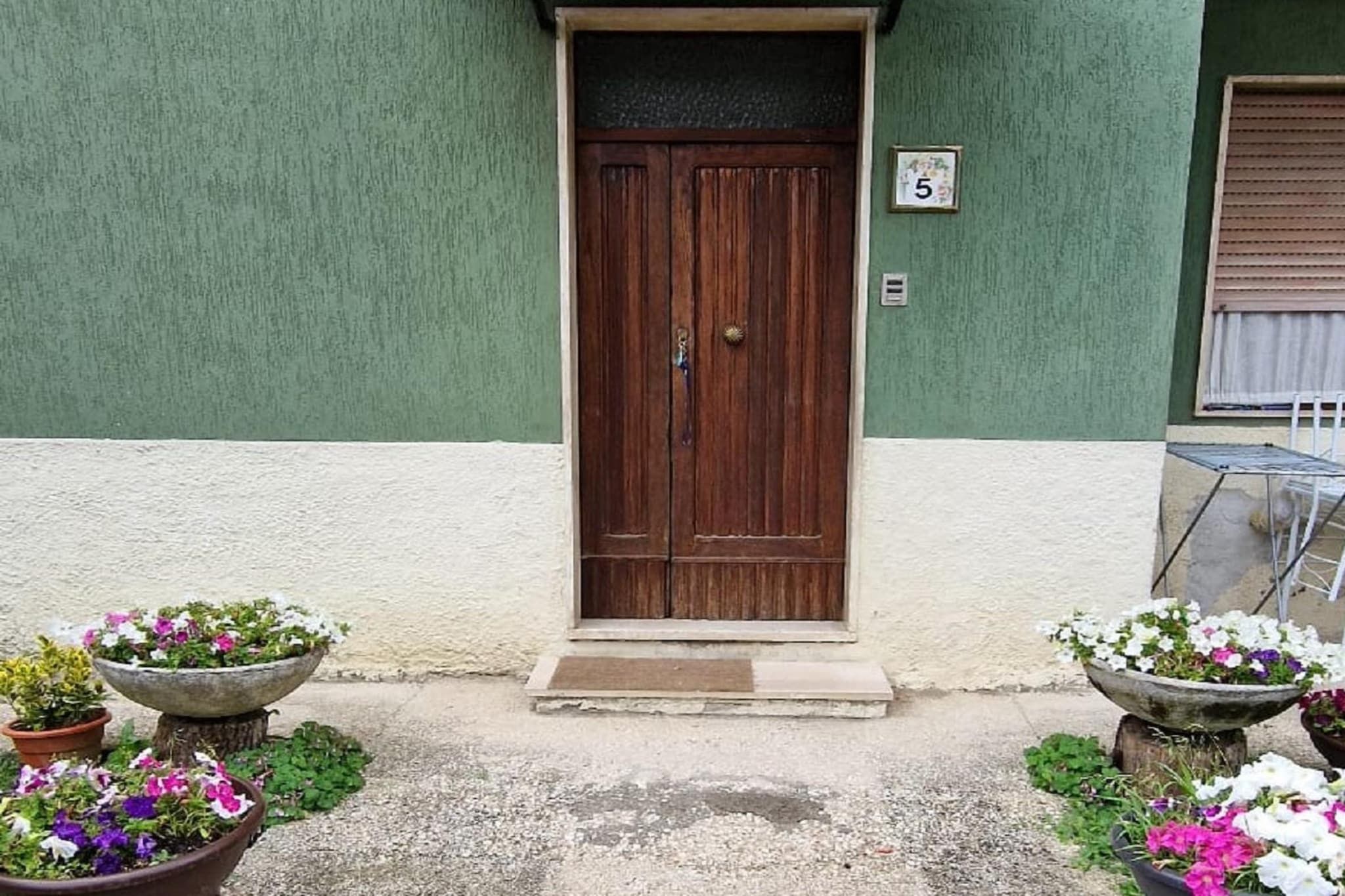 A two-story building with a green and white facade, a wooden door, and potted plants at the entrance.