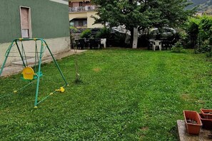 A grassy yard with a swing set and potted plants.