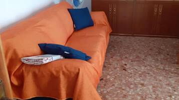 Una stanza con un divano arancione, un cuscino blu e una ventola.