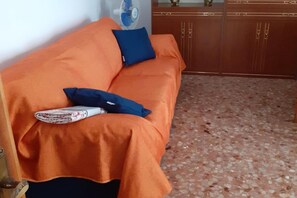 Una habitación con un sofá naranja, una almohada azul y un ventilador.