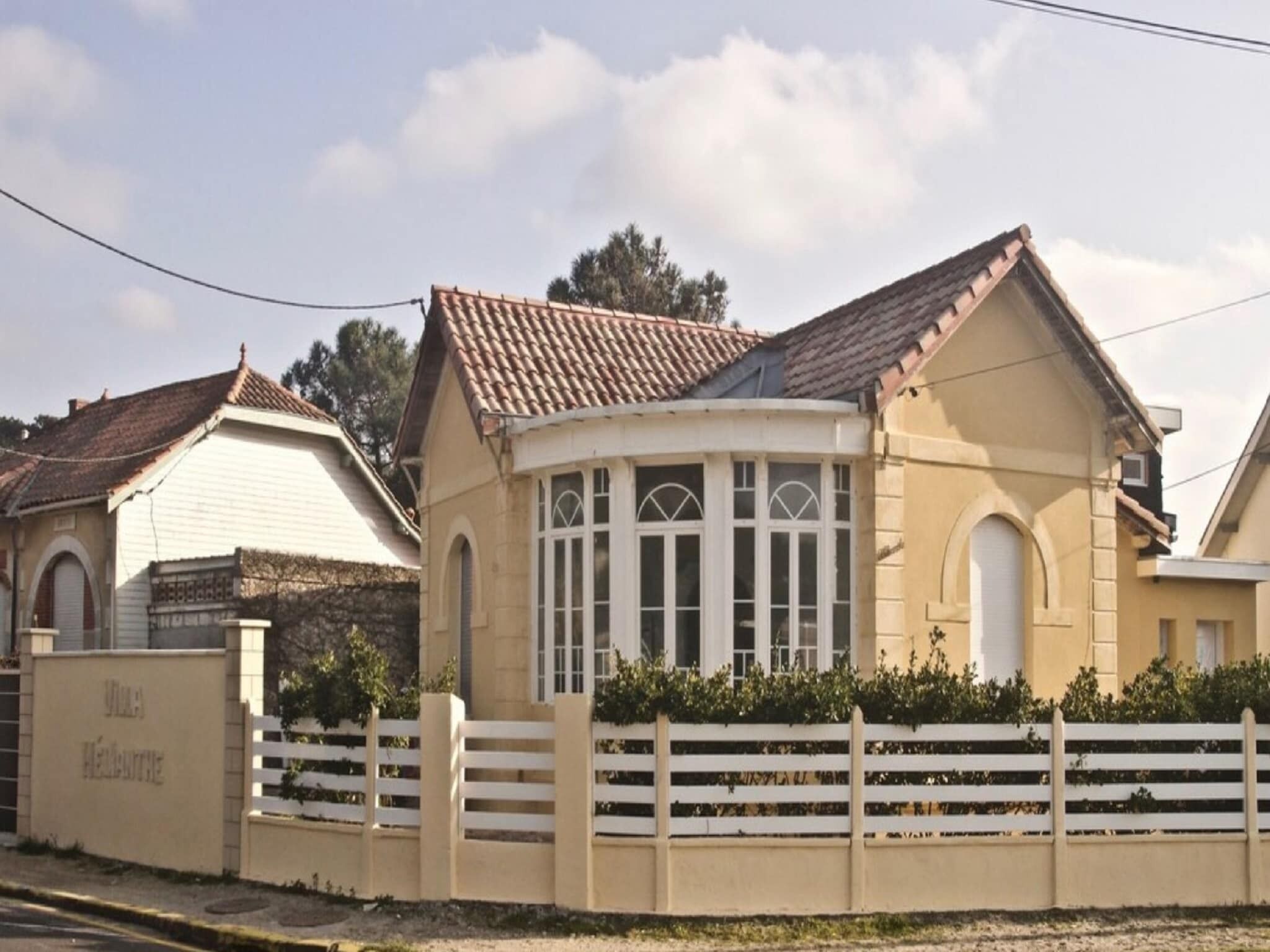 A beige building with a tiled roof, a white fence, and a small garden area.