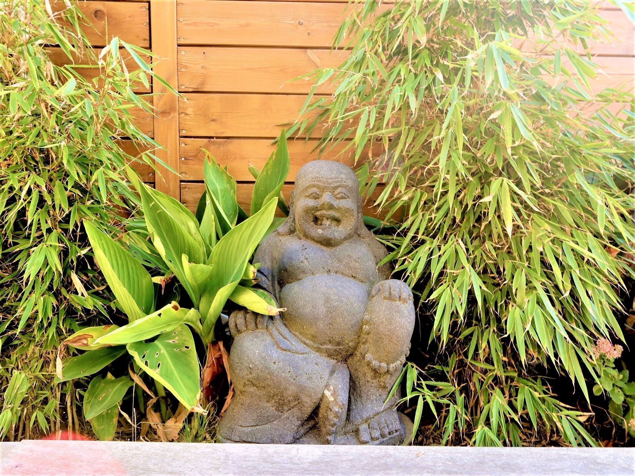 Une statue de pierre représentant une figure assise, entourée de plantes de bambou.