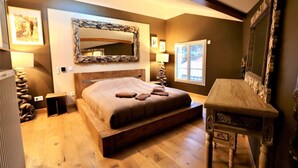 Un dormitorio con una cama grande, cabecera de madera, espejo con marco de piedra, una mesita y una ventana con vistas.