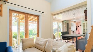 Ein gemütliches Wohnzimmer mit einem beigefarbenen Sofa, einem Esstisch mit Stühlen und einer großen Schiebeglas-Tür, die zu einem Garten führt.
