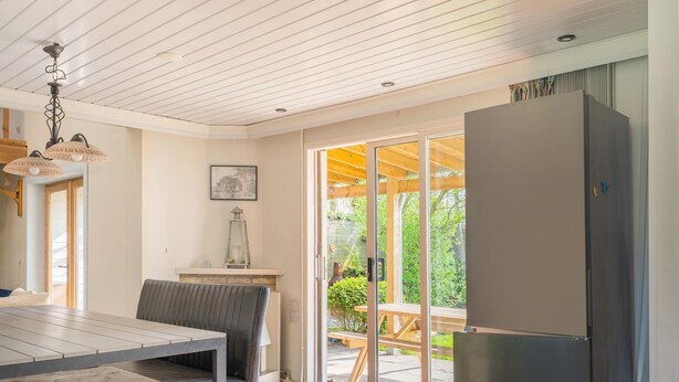 Eine moderne Küche mit einem großen Kühlschrank, einem Esstisch mit St ühlen und Blick durch die Glastür auf eine Terrasse.