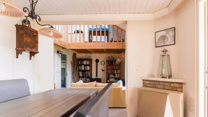 Ein gemütliches Wohnzimmer mit einem Holzesstisch, einer Couch und einem Kamin. Eine Treppe führt auf eine obere Ebene.