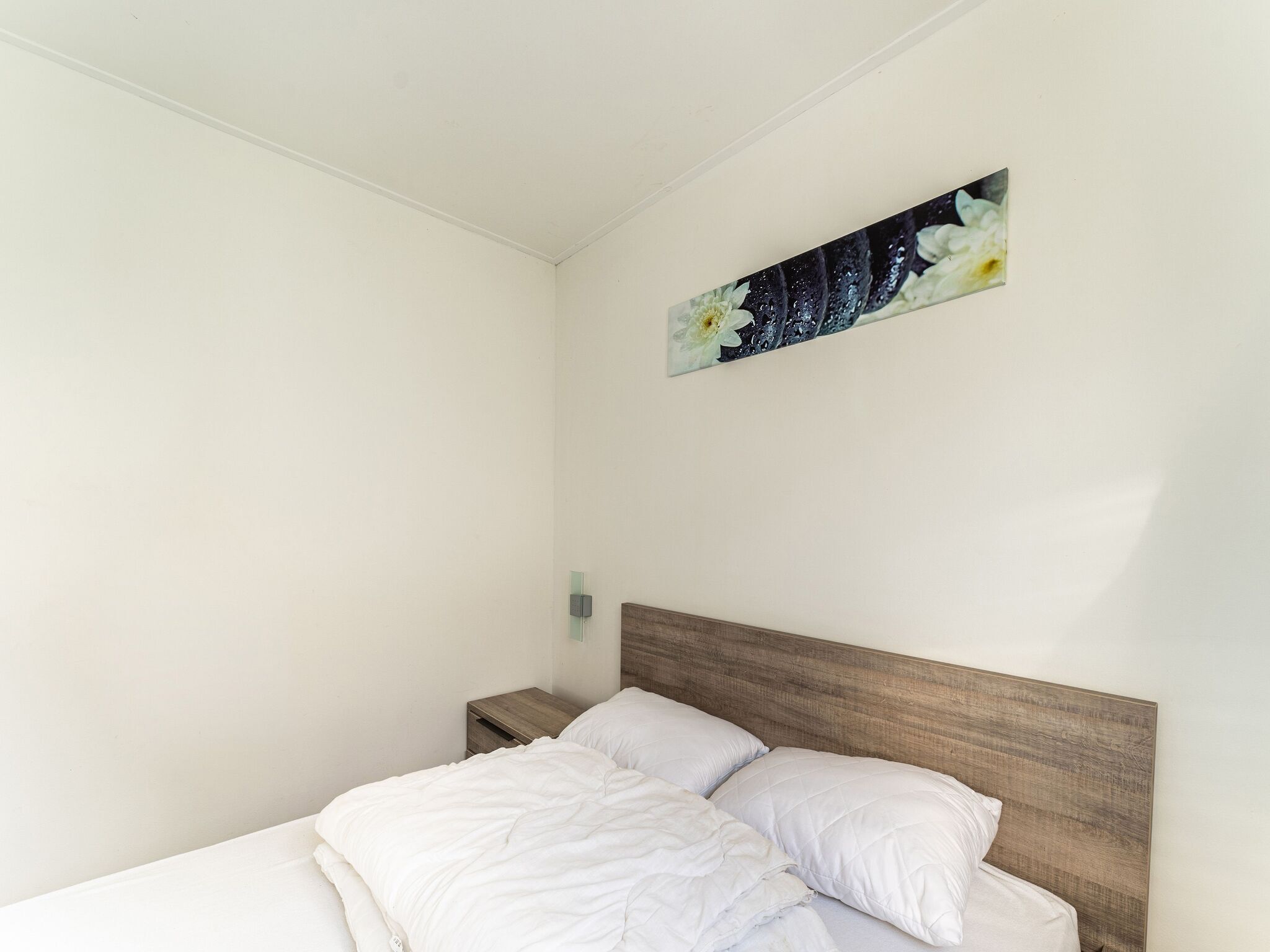 A bedroom with a wooden headboard, white bedding, and a wall-mounted painting of flowers.