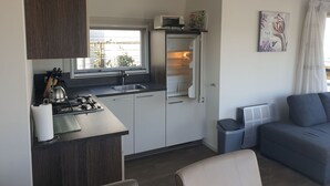 Cocina compacta con estufa a gas, pileta y refrigerador. Hay una ventana sobre la pileta, y se ve una pequeña estufa en el piso.
