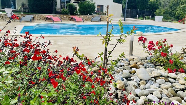A swimming pool surrounded by a stone patio, with red flowers in the foreground and a stone wall in the background. - Tranquil Villa with Pool (Lézignan-Corbières)