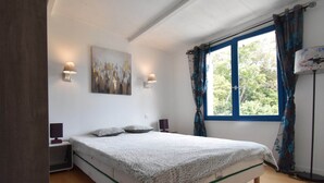 A bedroom with a bed, two bedside lamps, a painting on the wall, and a window with curtains. - Tranquil Villa with Pool (Lézignan-Corbières)