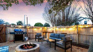 An outdoor patio area with a stone fire pit, a grill, and a seating arrangement including a sofa and chairs.