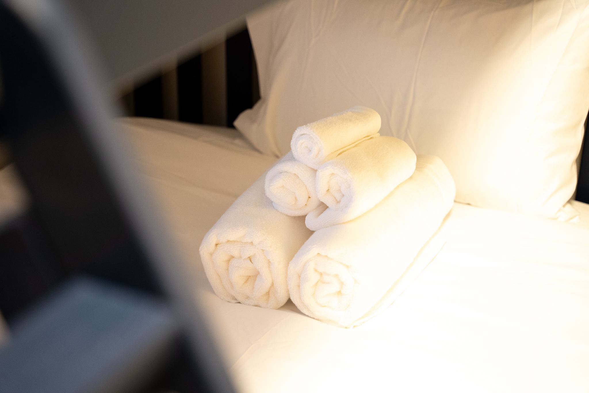 A bed with neatly rolled white towels and a pillow.