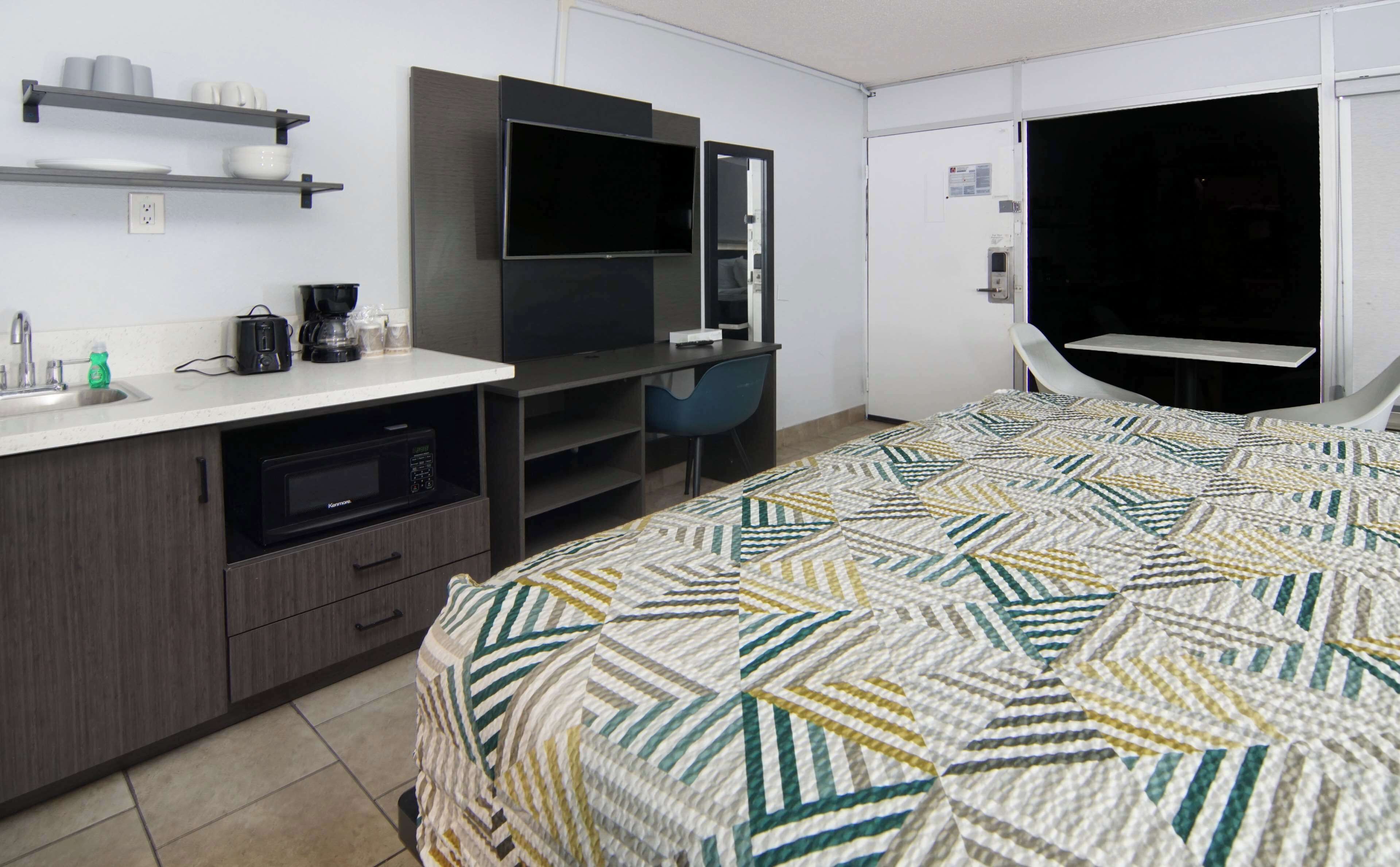 A hotel room with a bed, a kitchenette, a TV, and a desk.