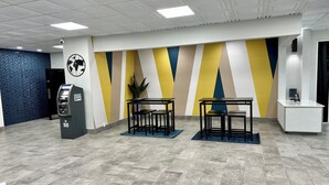 A modern lobby with a blue herringbone-patterned wall, a yellow and blue striped wall, a reception desk, a small plant, and an ATM. - Studio 6 Mesquite, Tx – Town East (Mesquite)