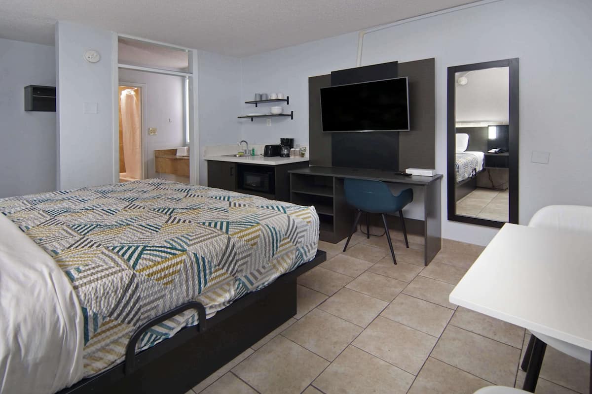 A hotel room with a bed, a desk, a chair, a TV, and a mirror.