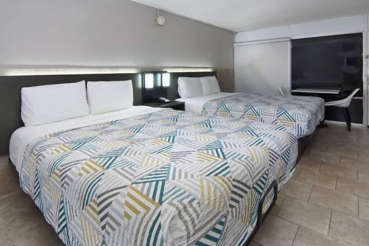 A hotel room with two beds, a desk, and a TV.