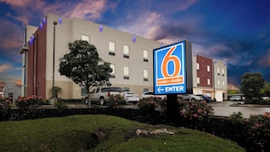 A 6 Motel & Studio building with a large entrance sign, parking lot, and surrounding greenery.