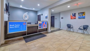A hotel reception area with a modern design, featuring a reception desk, a large illuminated number '6', and a digital screen displaying a promotional message.
