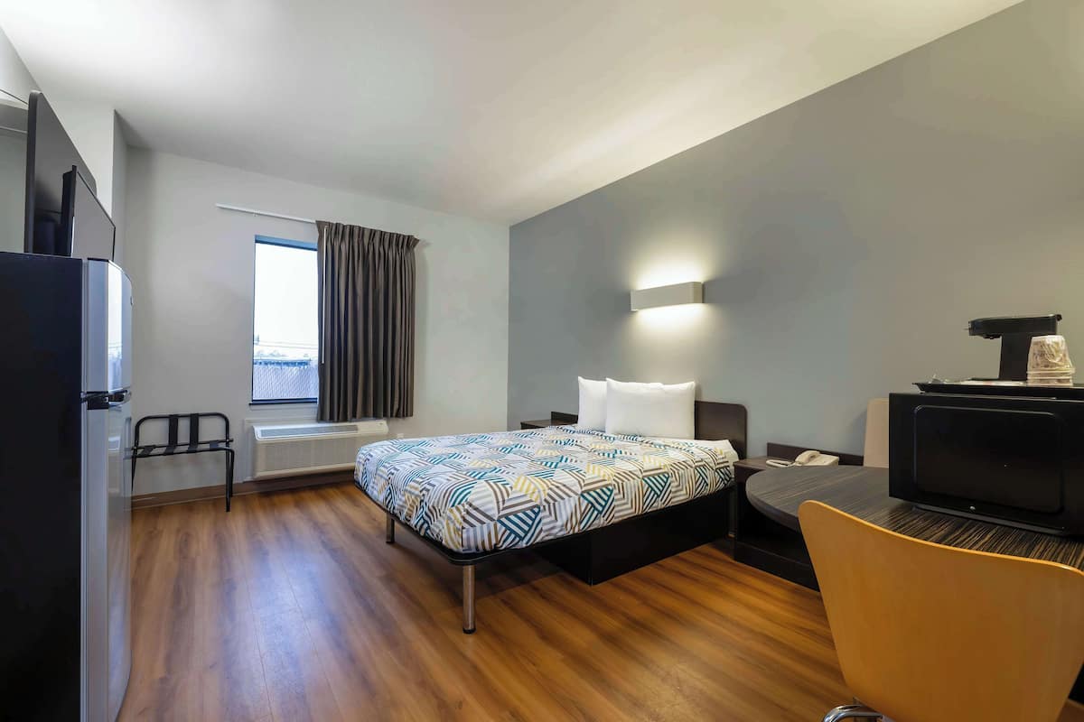 Ein Hotelzimmer mit Bett, Schreibtisch, Stuhl, Fernseher und einem Fenster mit Vorhängen.