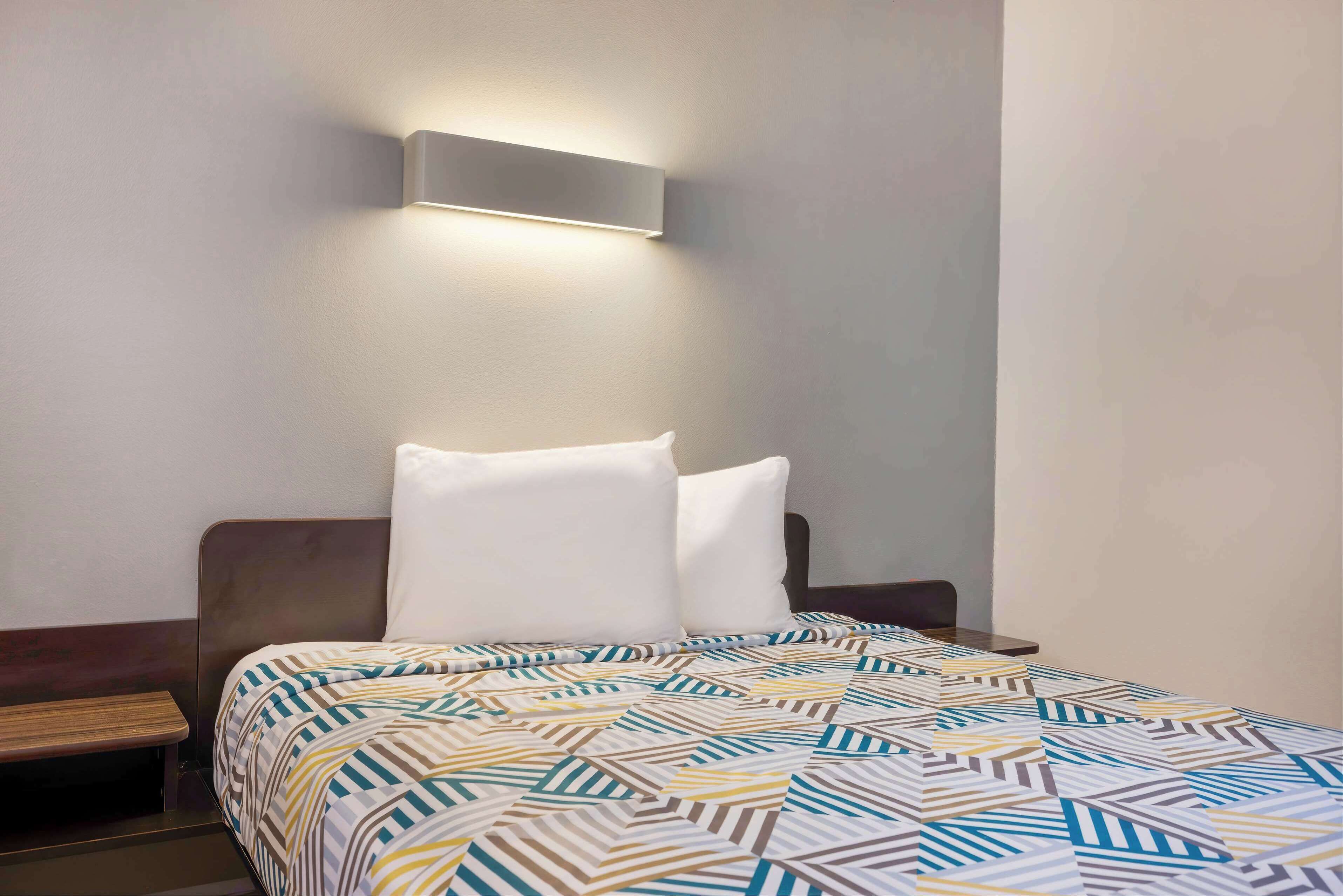 A neatly made bed with a patterned bedspread, a bedside table, and a wall-mounted light fixture.