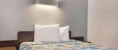 A neatly made bed with a patterned bedspread, a bedside table, and a wall-mounted light fixture.
