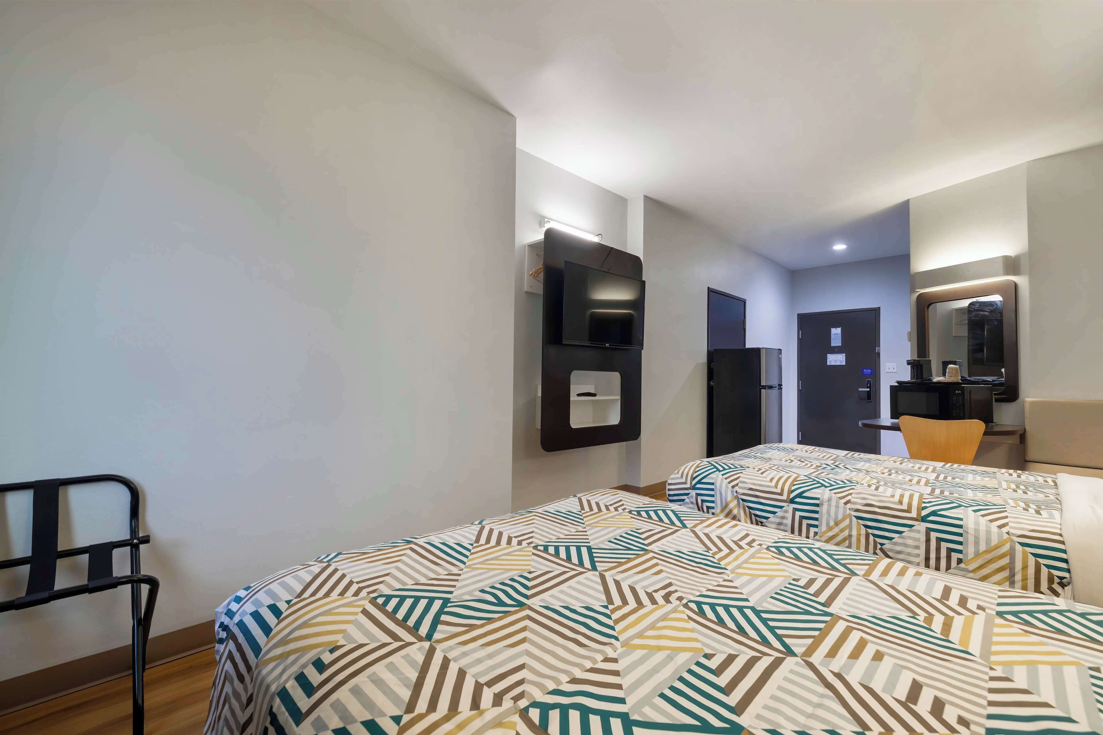 Ein Hotelzimmer mit zwei Betten, einem an der Wand befestigten Fernseher, einem Schreibtisch mit Stuhl und einem Spiegel.