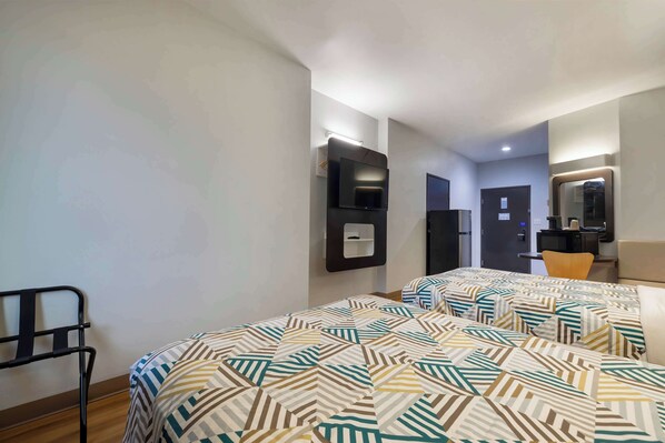 A hotel room with two beds, a TV mounted on the wall, a desk with a chair, and a mirror.
