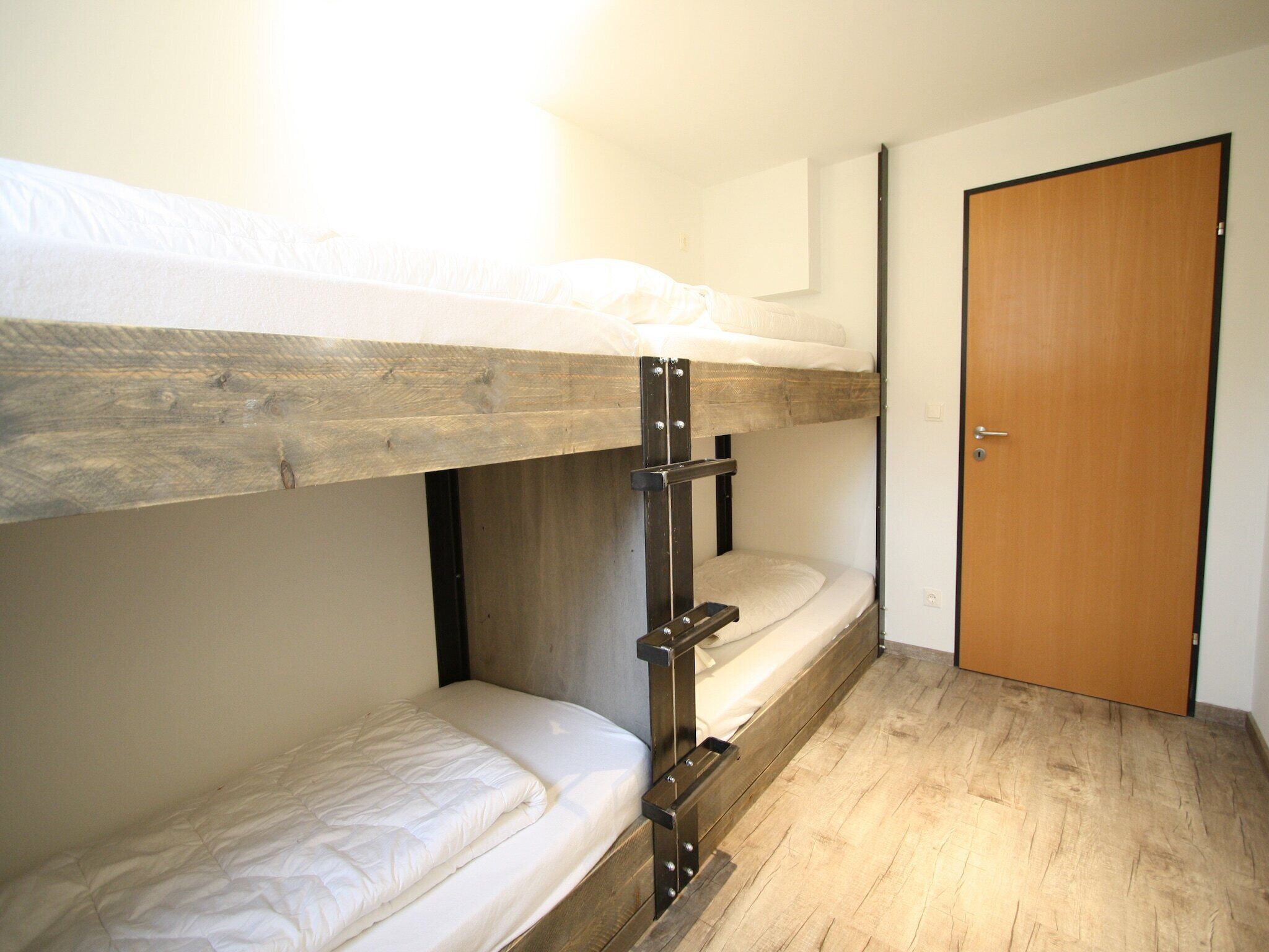 A bunk bed room with a wooden floor and a closed door.