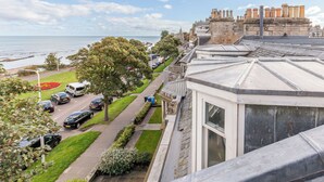 A coastal building with a view of the sea, a parking lot, and a pathway lined with trees. - Beachfront Penthouse by the Old Course (The Scores St Andrews)