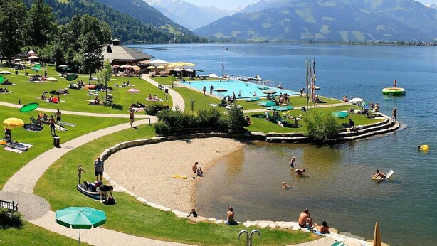 Un complejo turístico junto al lago con piscina, tumbonas y un pequeño embarcadero.