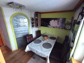 Un coin repas avec une table dressée pour deux personnes, un meuble en bois orné d’objets décoratifs et un mur sur lequel est accrochée une grande peinture florale.