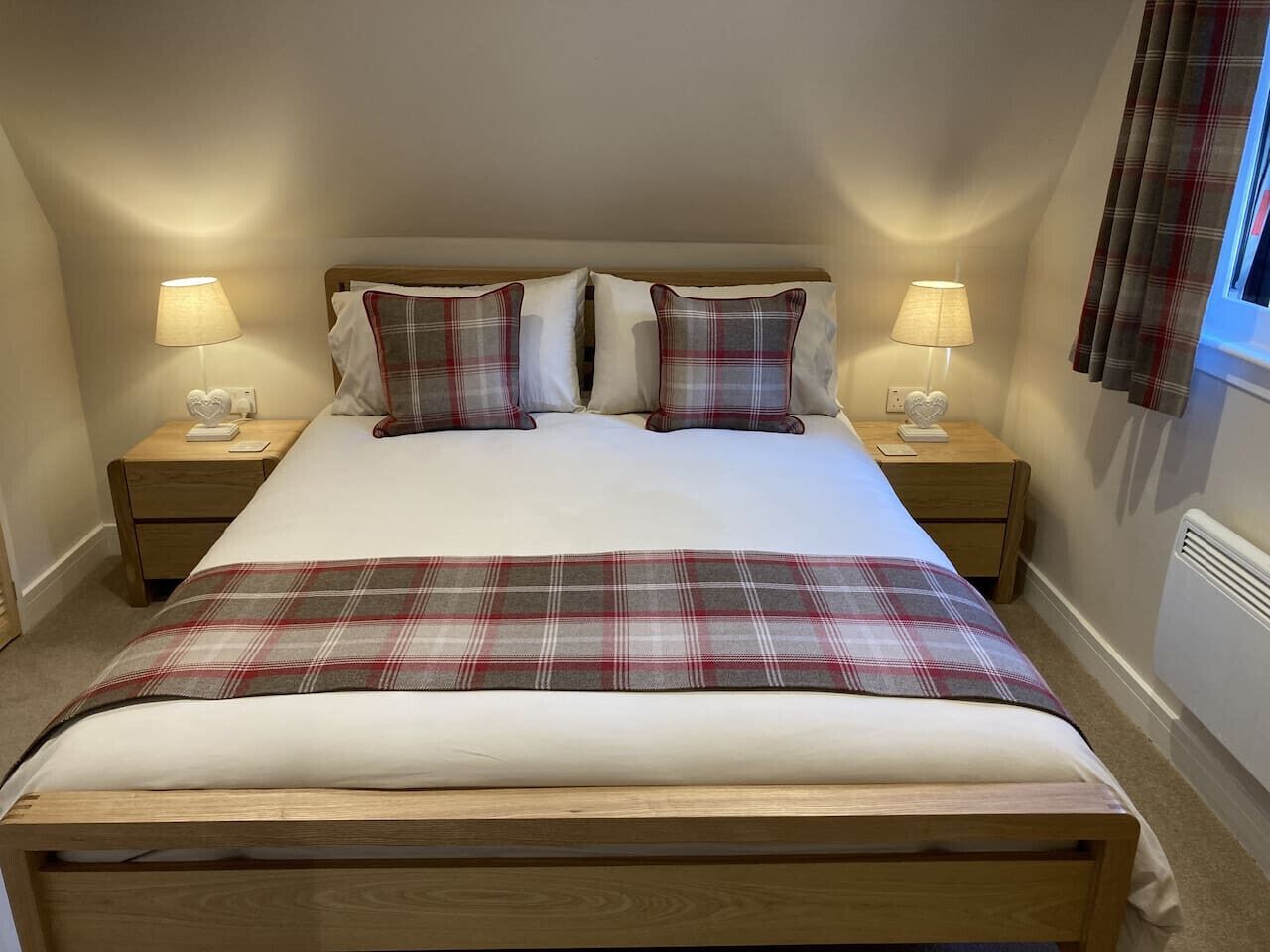 Quarto com uma cama grande, duas mesas de cabeceira com luminárias, um cobertor xadrez e uma janela com cortinas.