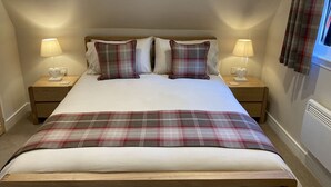 Un dormitorio con una cama grande, dos mesitas de noche con lámparas, una colcha a cuadros y una ventana con cortinas.
