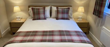 Quarto com uma cama grande, duas mesas de cabeceira com luminárias, um cobertor xadrez e uma janela com cortinas.