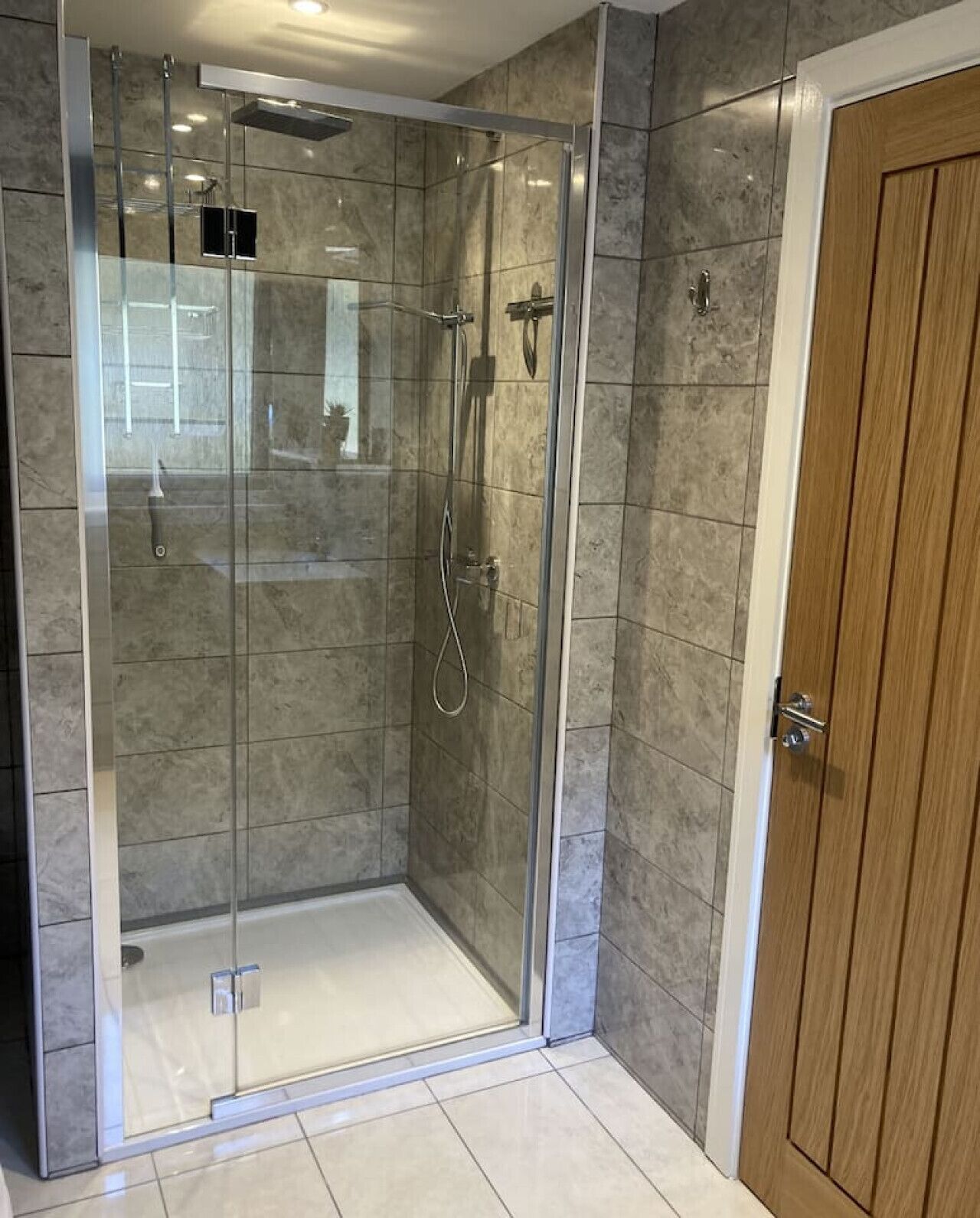 A glass-enclosed shower with a tiled floor and a wooden door.