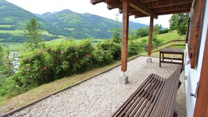 A covered outdoor seating area with a bench and table, overlooking a scenic valley with mountains and a river. - Chalet in Niedernsill near Zell am See Ski Area (Niedernsill)