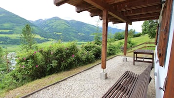 Un espace extérieur aménagé, abrité et doté d’un banc et d’une table, offrant une vue panoramique sur une vallée pittoresque, avec des montagnes et une rivière.