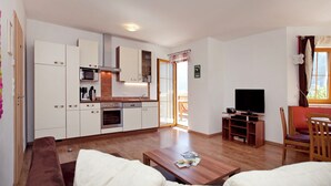 Una sala de estar moderna con un sofá, una mesa de centro y un televisor. Cuenta con una zona de cocina con armarios y electrodomésticos.