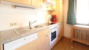 A compact kitchen with wooden cabinets, a built-in oven, a coffee maker, and a window with curtains. - Chalet in Austria near Ski Slopes & Nature (Mittersill)