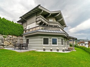 Une maison à plusieurs étages avec un mur en pierre, un balcon et une cour gazonnée.