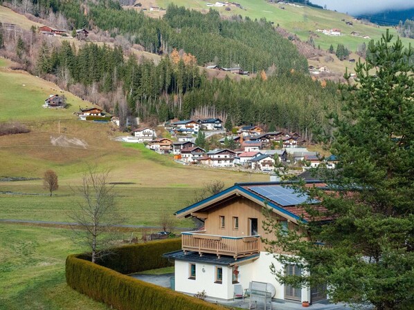 Un village perché sur une colline, avec des maisons traditionnelles, une imposante maison en bois dotée d’un balcon, et une vue dégagée sur la forêt environnante.