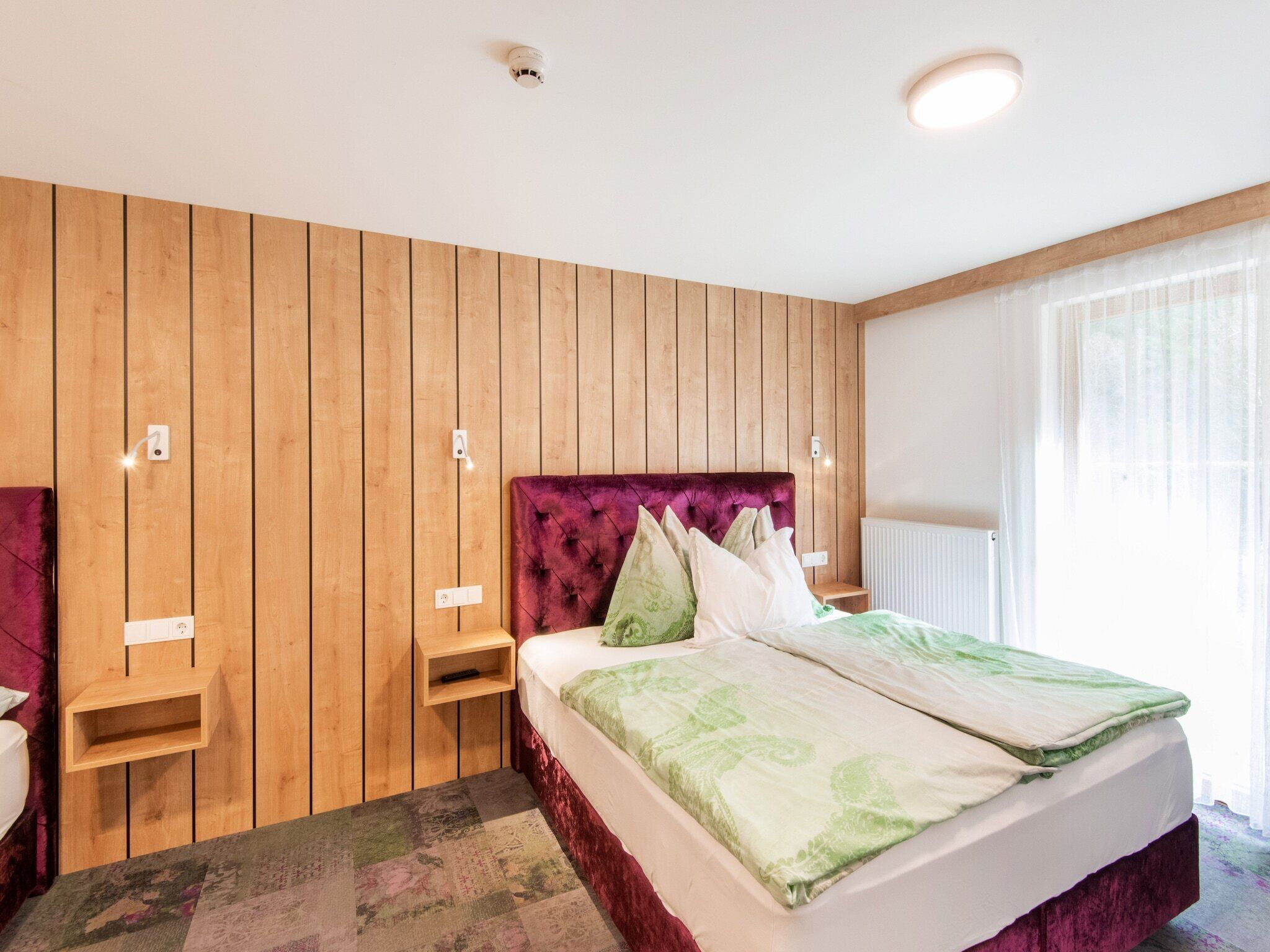Ein Hotelzimmer mit einer holzverkleideten Wand, einem gesteppten Kopfteil, einem Bett mit grün-weißer Bettwäsche, einem Nachttisch und einer Nachttischlampe.