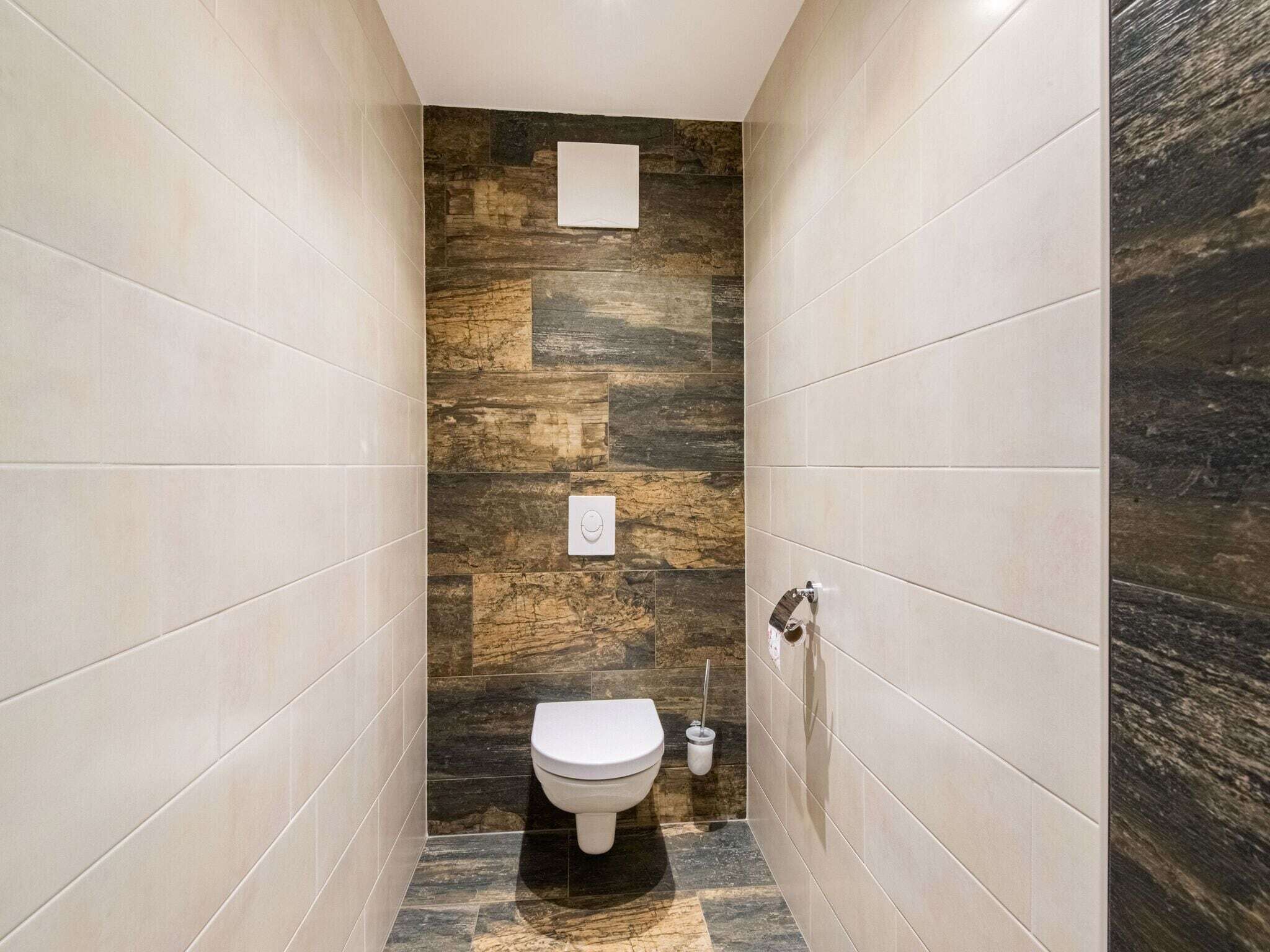 Une salle de bain moderne avec un mur d’accent en pierre, des toilettes et un sèche-mains.
