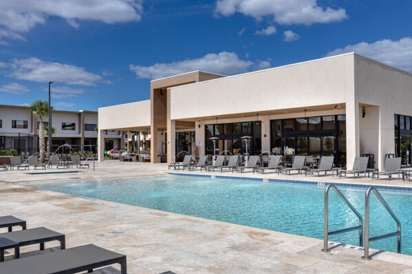 Un hotel moderno con piscina, sillones de descanso y un cielo azul despejado.