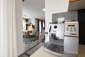Een moderne keuken met een ingebouwde koffiemachine, een eethoek met een houten tafel en stoelen, en een trap die leidt naar een ander niveau.