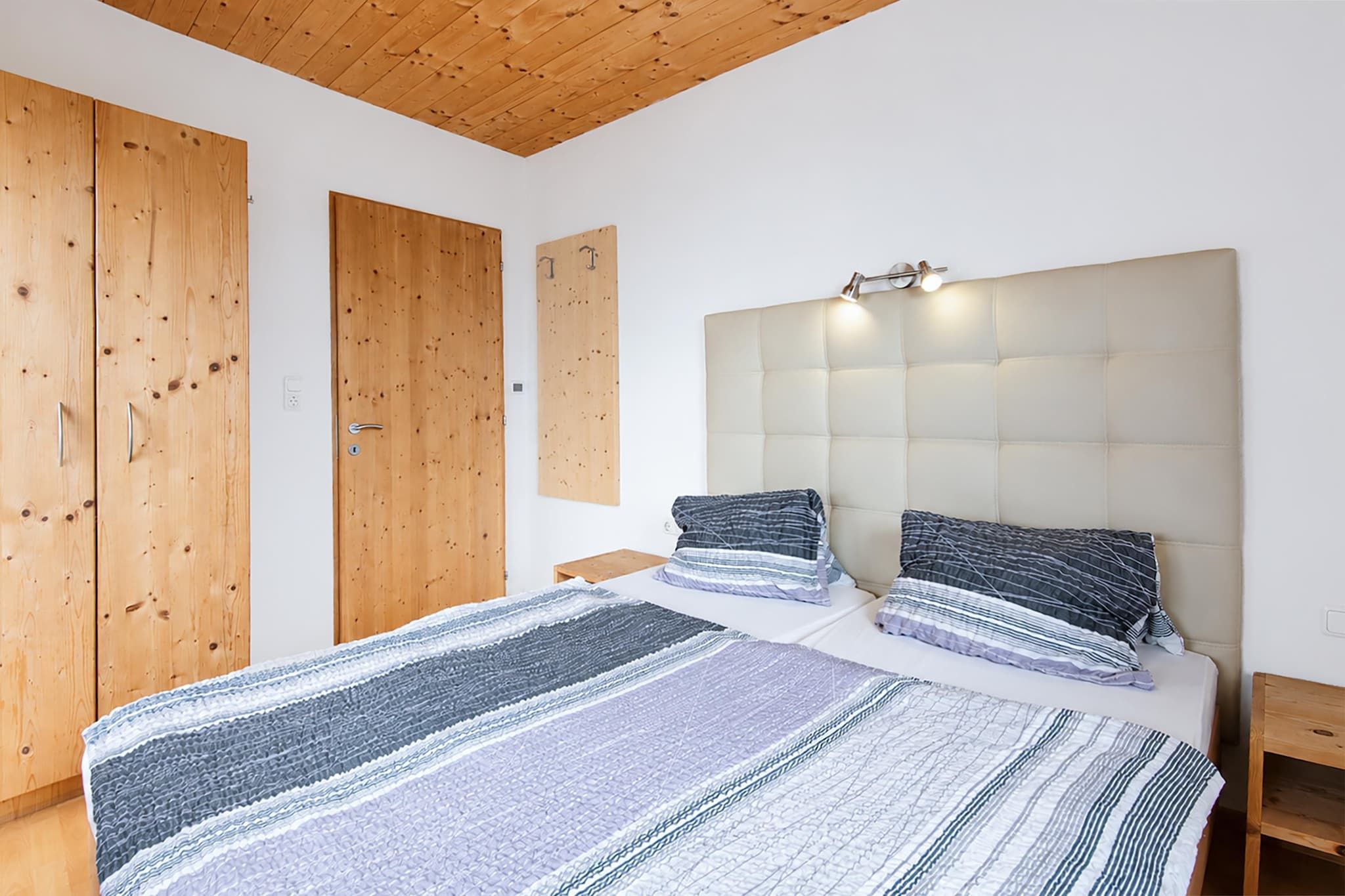 A bedroom with a large bed, wooden wardrobe, and a headboard with lights.
