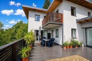 A modern two-story house with a balcony, potted plants, and outdoor furniture.
