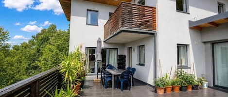 Une maison moderne dotée d’un balcon, de plantes en pot et d’un coin repas.