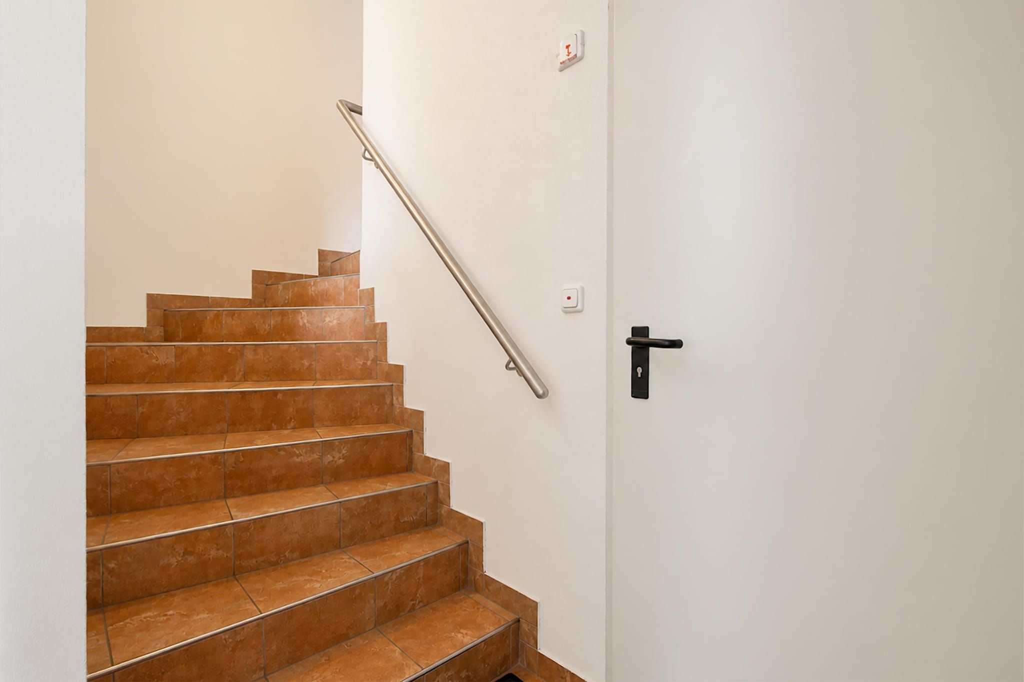 Un escalier avec une rampe menant à une porte dotée d’une poignée noire.